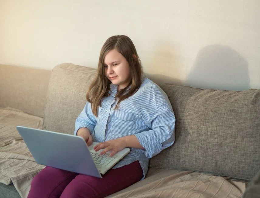 Disabled girl sitting on sofa at home using laptop to look up H3 Care