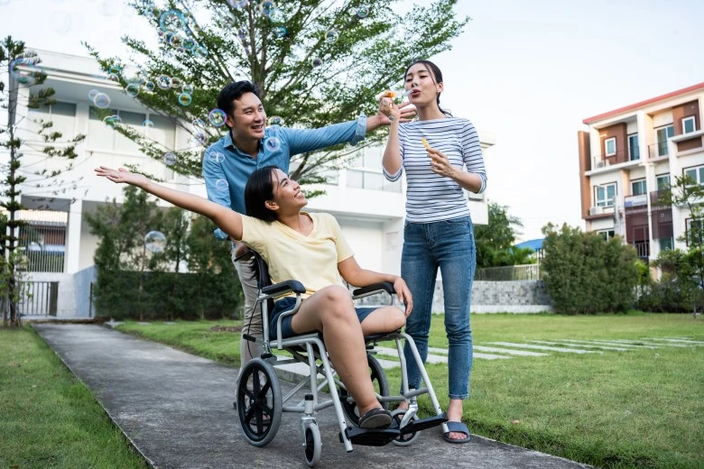 Disabled woman in wheelchair outside blowing bubbles with two support workers